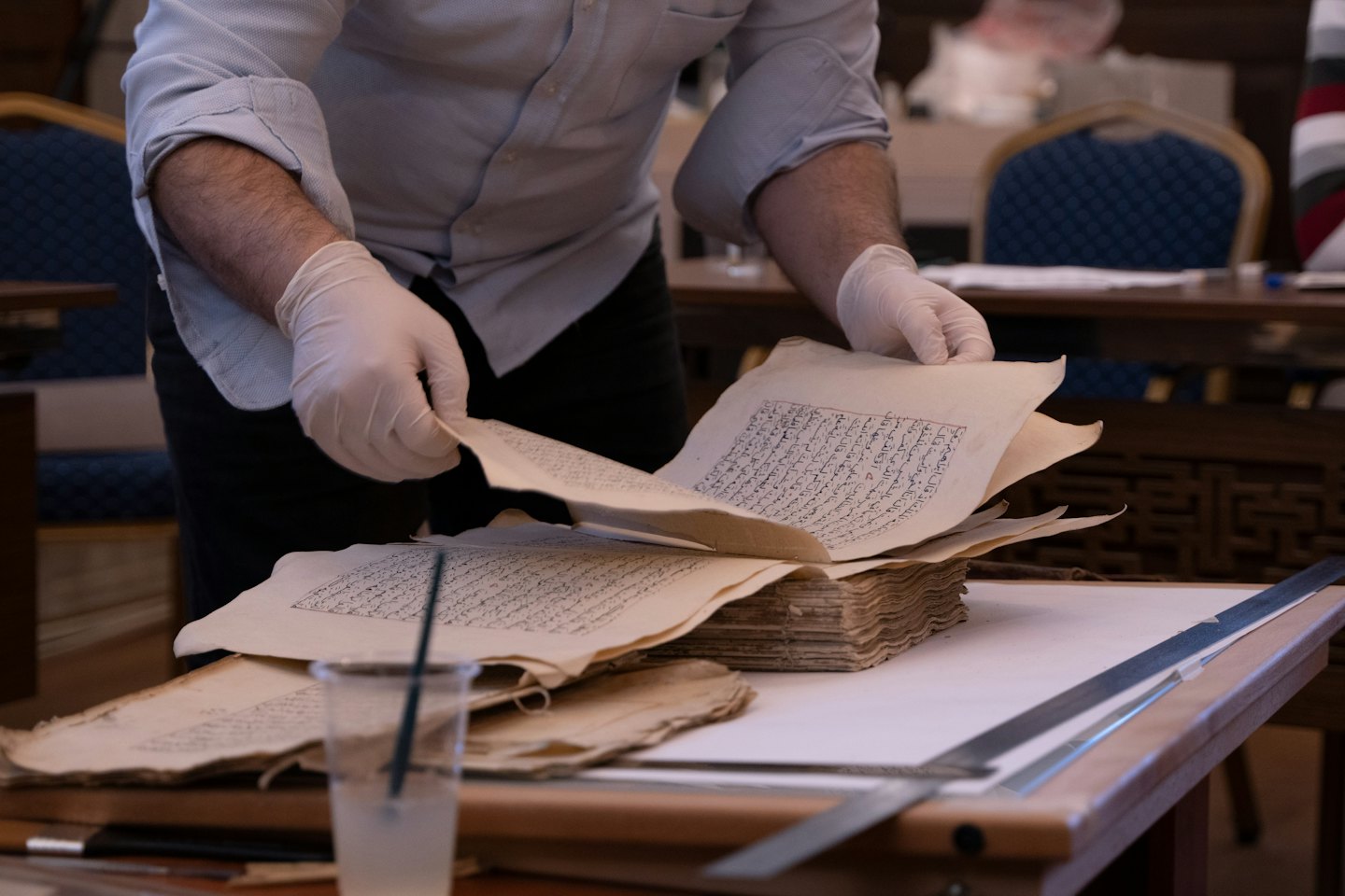 Archivist in gloves examines old handwritten documents.