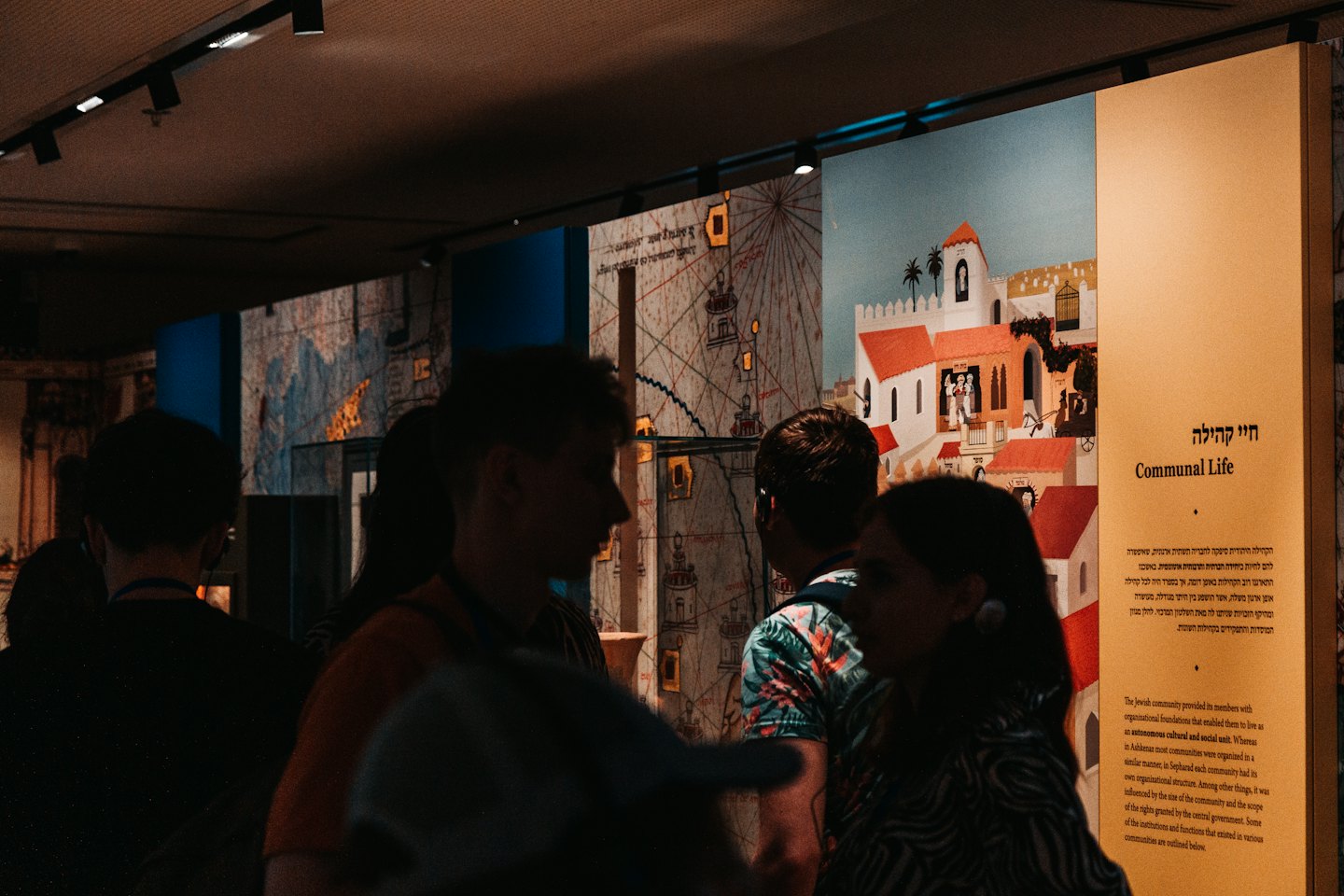 Visitors examining historical maps and town illustrations in a museum exhibit.